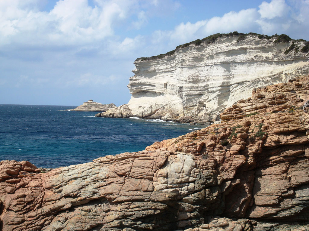 Falaises érodées de calcaire blanc datant du miocène, la base plus fragile est riche en sable.
Le contact entre les molasses blanches  du miocène et le granite du socle au premier plan est bien visible.