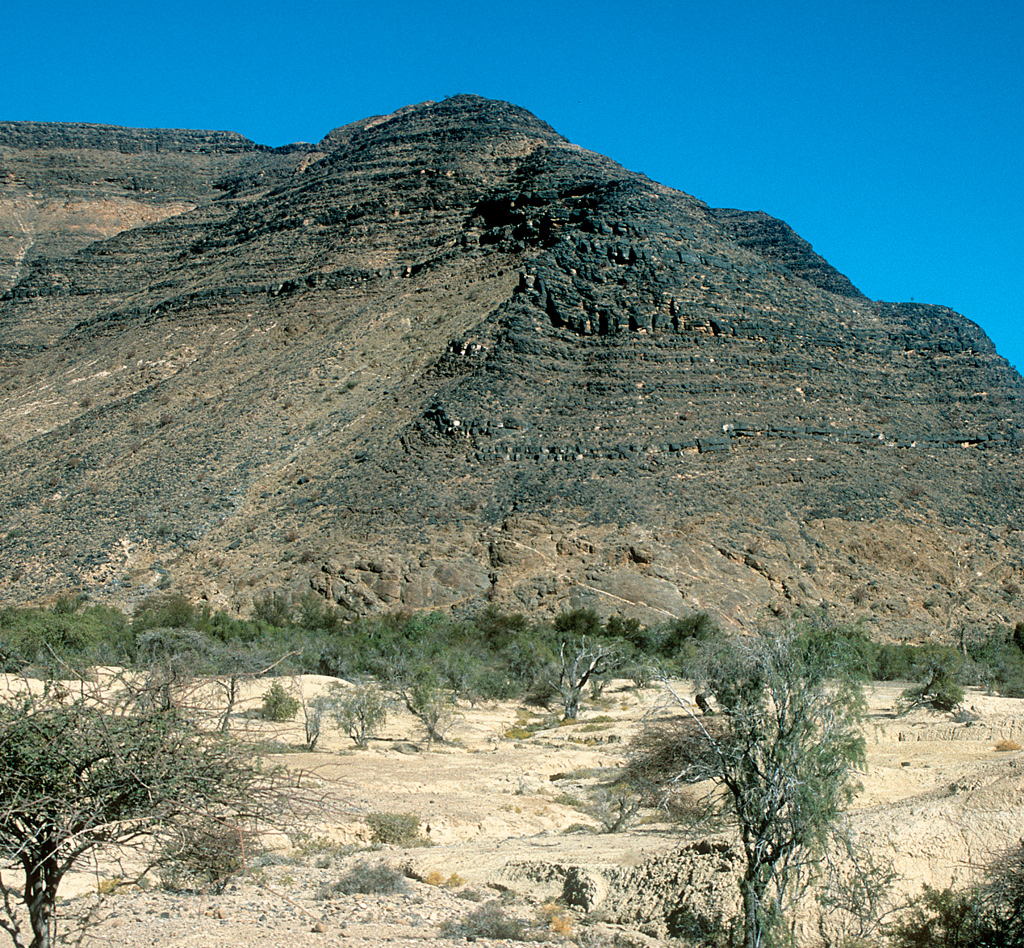 Photo prise dans les Zaris montains, près de Sossusvlei, en bordure du désert du Namib. Au dessus et en sombre on trouve des boues calcaires très riches en dépôts organiques (noir car déposé en domaine anaérobie). On appelle ce niveau la "Schwarzkalk", il fait partie du Nama group avec un age de 600 Ma.  La couche du dessous est du socle de 1,5 milliards d'années. C'est du socle composé de gneiss (la Rehoboth sainclair sequence). La limite entre les 2 couches est la pénéplaine d'une ancienne chaine de montagnes.    On voit sur cette photo une faille inverse et donc aussi une discordance de 800 millions d'années!