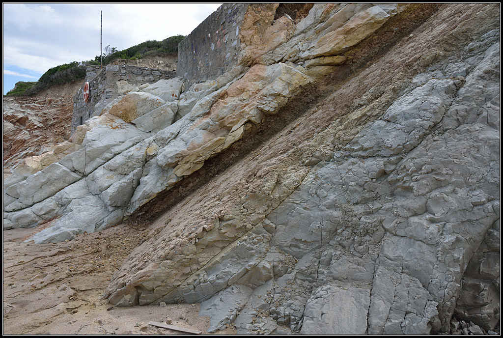 Limite Crétacé - Tertiaire à Bidart.
La couche d'argile (noire à la base, rouge au dessus) sépare les marnes datées du Maastrichtien (à droite) des calcaires roses et blancs datés du Danien (à gauche). La partie noire de la couche argileuse est très riche en iridium.<br />
<a href='https://phototheque.enseigne.ac-lyon.fr/photossql/photos.php?RollID=images&FrameID=K-T-Bidart-legendes'>Avec légendes</a>.