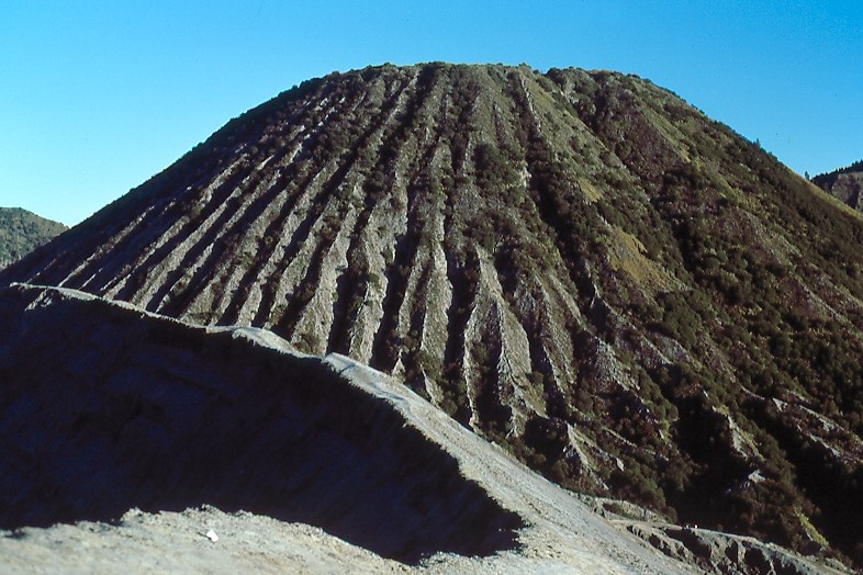 Dans la caldeira du Tengger, vaste mer de sable volcanique de 9 km de diamètre, le volcan Batok, observé depuis le bord du cratère du <A HREF='https://phototheque.enseigne.ac-lyon.fr/photossql/photos.php?RollID=images&FrameID=bromo'>Bromo</A>, montre ses flancs striés par l'érosion.  <BR><A HREF='https://phototheque.enseigne.ac-lyon.fr/photossql/GoogleEarth/batok.kmz'>  <IMG SRC='googleearth.gif' BORDER=0>  </A>