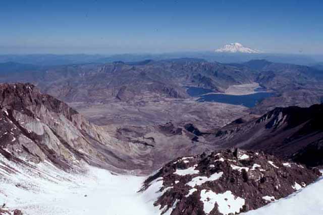 Le dôme du Mont Saint Helens et le cratère d'explosion vus de la lèvre sud du sommet. Au deuxième plan, le lac Spirit et au fond le Mont Rainier.  Le Mont Rainier est un volcan de la chaîne des Cascades (état de Washington, USA), il donne une image proche de celle du Mont Saint Helens avant l'éruption.
<BR><A HREF='https://phototheque.enseigne.ac-lyon.fr/photossql/GoogleEarth/dome_helens.kmz'><IMG SRC='googleearth.gif' BORDER=0></A>