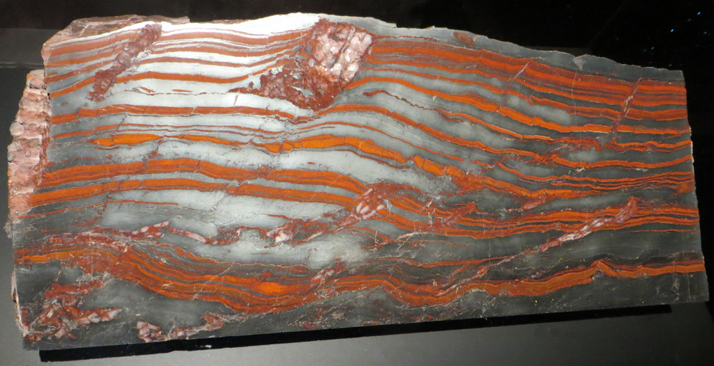 Alternance de lits de quartz et de fer oxydé (-2,1 milliards d'années, Précambrien, Michigan, Etats-Unis). La grande majorité des minerais de fer du monde est constituée de ce qu'on appelle des fers rubanés ( Banded Iron Formation ou BIF, en anglais). Ces BIF existent avec plusieurs faciès, mais le faciès « classique » est constitué d'alternances de lits de silice (plus ou moins ferrugineuse) et d'hématite (Fe<sub>2</sub>O<sub>3</sub>, oxyde ferrique où le fer est sous sa forme la plus oxydée Fe<sup>3+</sup>). Ce sont toujours des formations sédimentaires marines.  Ils seraient dus à l'oxydation générale de l'eau de mer par l'atmosphère devenant elle-même riche en 0<sub>2</sub> à cette époque, à cause de l'oxygène produit par les bactéries. 
