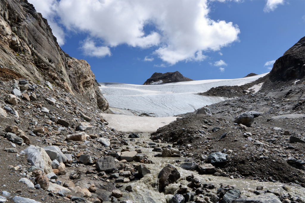 Glacier de Rhêmes-Golette, au fond de la vallée de la grande Sassière, dans les Alpes.
Au premier plan, ruisseau provenant de la fonte de la glace. La couleur brune de l'eau témoigne de l'activité érosive. Plan moyen : névé. Arrière plan : glacier. Le recul important du glacier (plus de 300 m durant les cinquante dernières années) met à l'affleurement les roches qui se trouvent normalement sous la glace.
