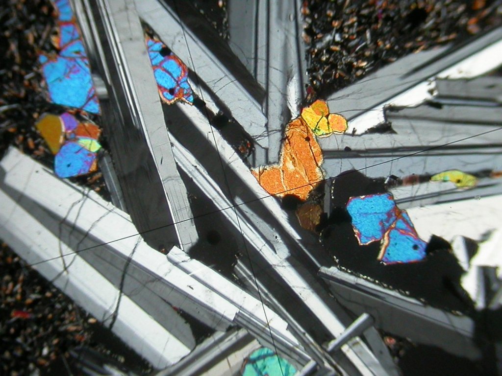 Lame mince de basalte observée en lumière polarisée analysée. De gros cristaux de plagioclases occupent le centre de l'écran. Des cristaux d'olivine de couleurs vives sont également visibles.