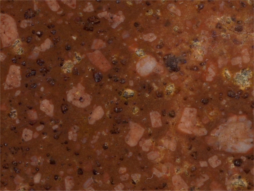 Echantillon de rhyolite du Mâconnais, surface polie scannée. La matrice est colorée en rouge par les oxydes de fer. Les minéraux visibles sont le quartz, le feldspath orthose et d'anciennes biotites transformées en chlorites.